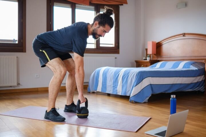 Man leaning over to hold kettlebell on the floor, the starting position for the kettlebell clean