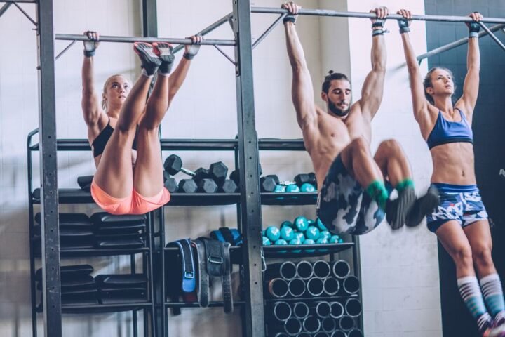 Three people performing toes-to-bar exercise in the gym