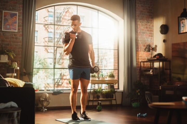 Man performs biceps curl with dumbbells in living room