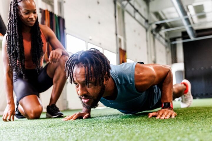 Man performs push-up in gym, a woman kneels beside him