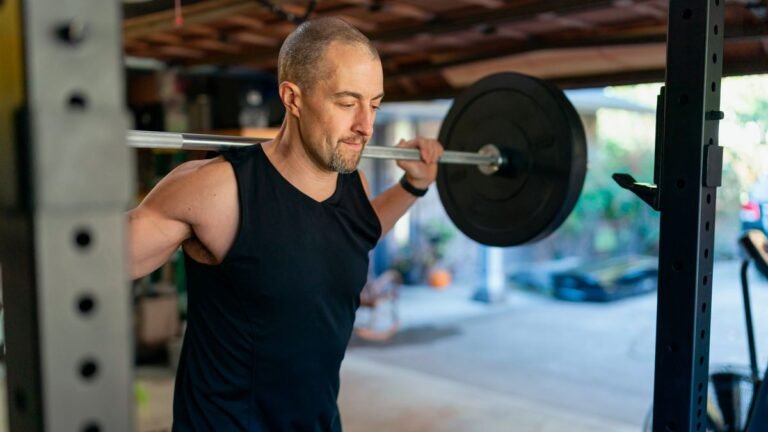 Man in his garage gym with a barbell over his shoulders next to a squat rack