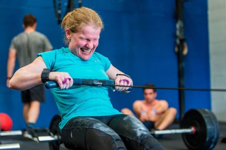 Woman in CrossFit gym rowing, face contorted with effort