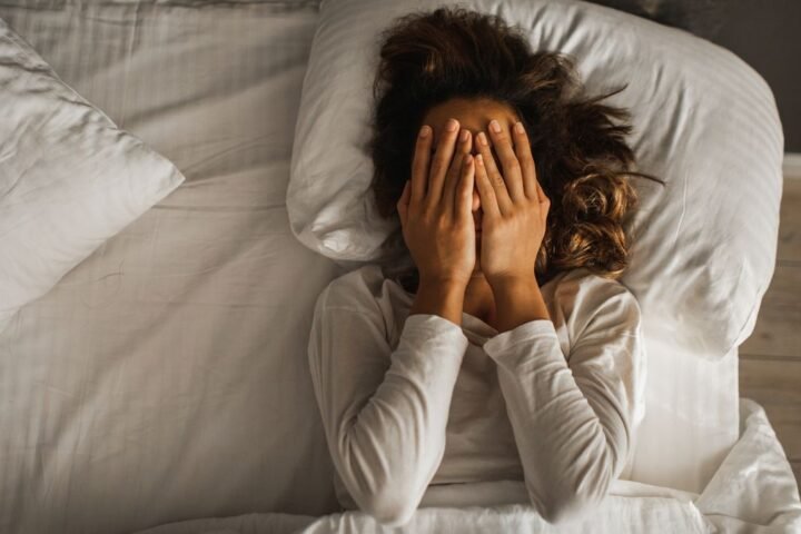 Woman lying in bed covering her face with her hands