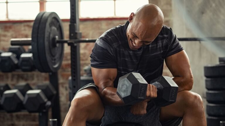 Man grimacing with effort as he performs a concentration curl in a gym